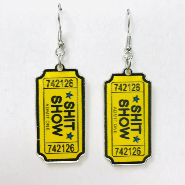 Acrylic earrings shaped like yellow admission tickets with "SHIT SHOW" text and blue stars.