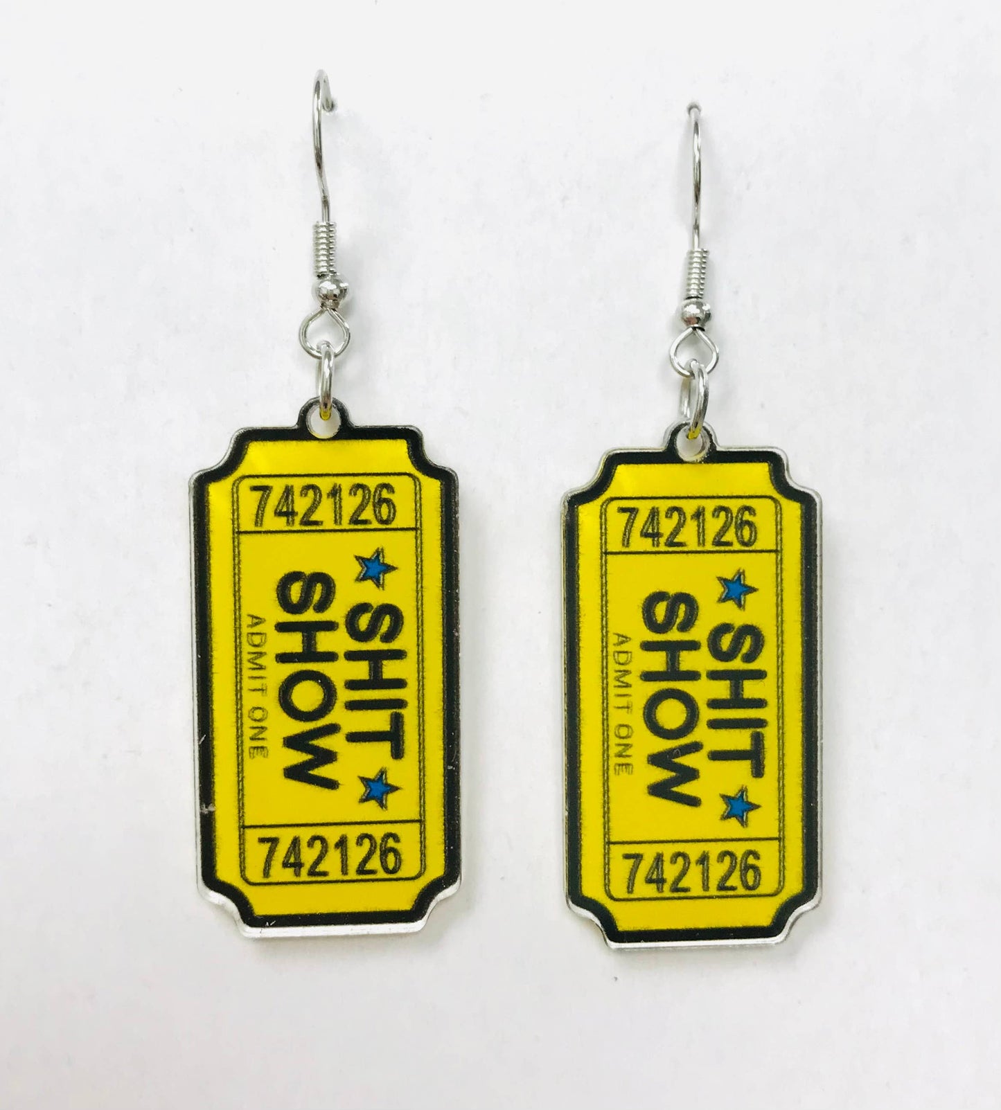 Acrylic earrings shaped like yellow admission tickets with "SHIT SHOW" text and blue stars.