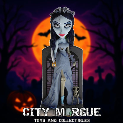 Royal Bobbles Emily bobblehead in a gray dress, standing in front of a grave with a spooky background.